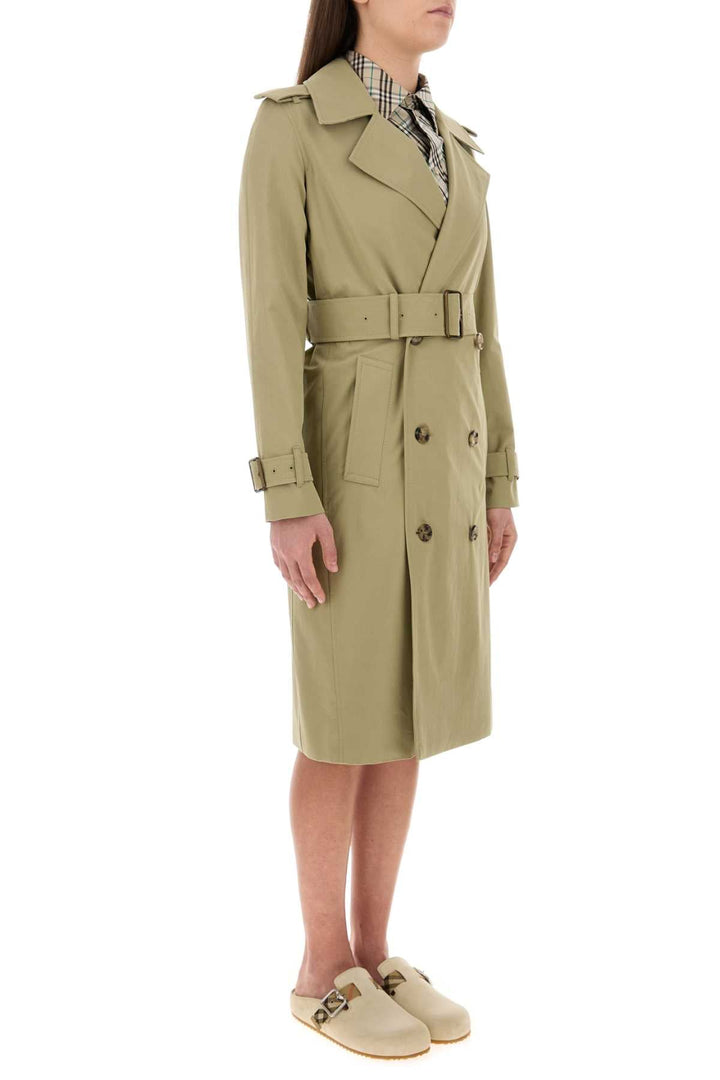Person wearing a sage green trench coat on a white background