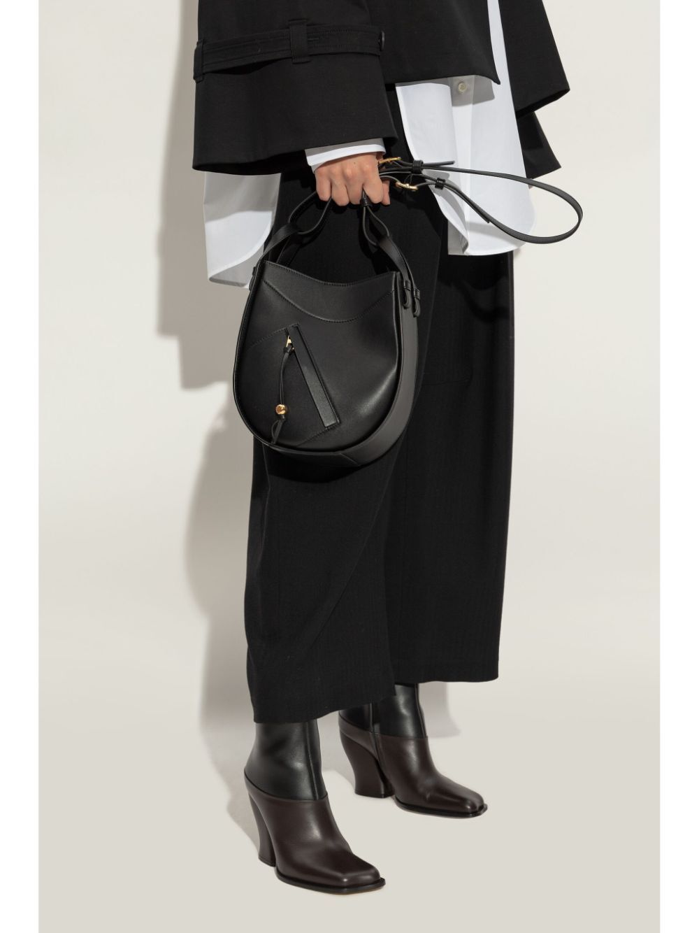 Person holding a black leather handbag against a white background