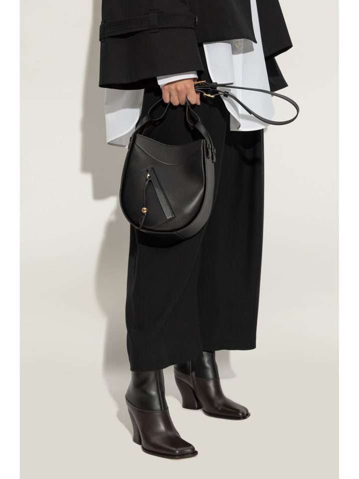 Person holding a black leather handbag against a white background