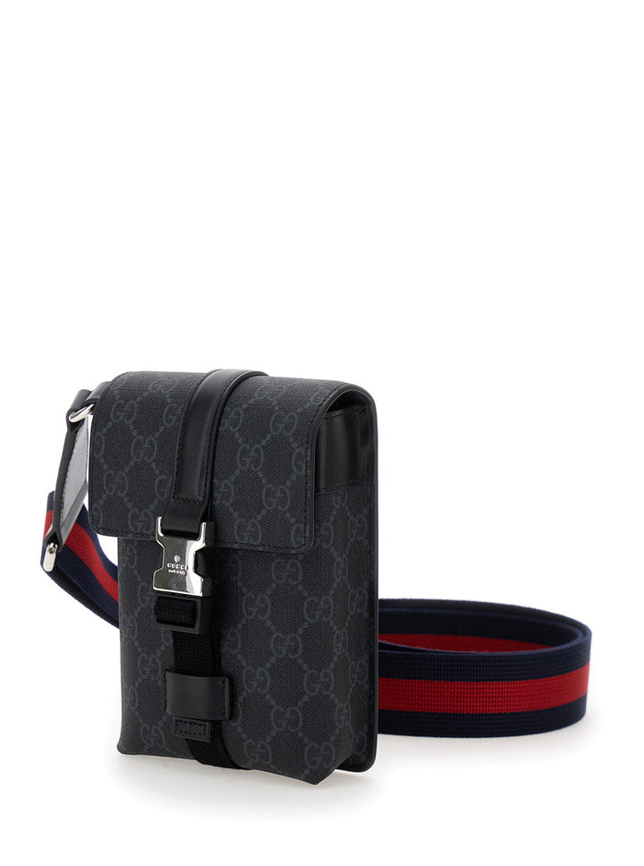 Black patterned crossbody bag with a red and blue strap on a white background