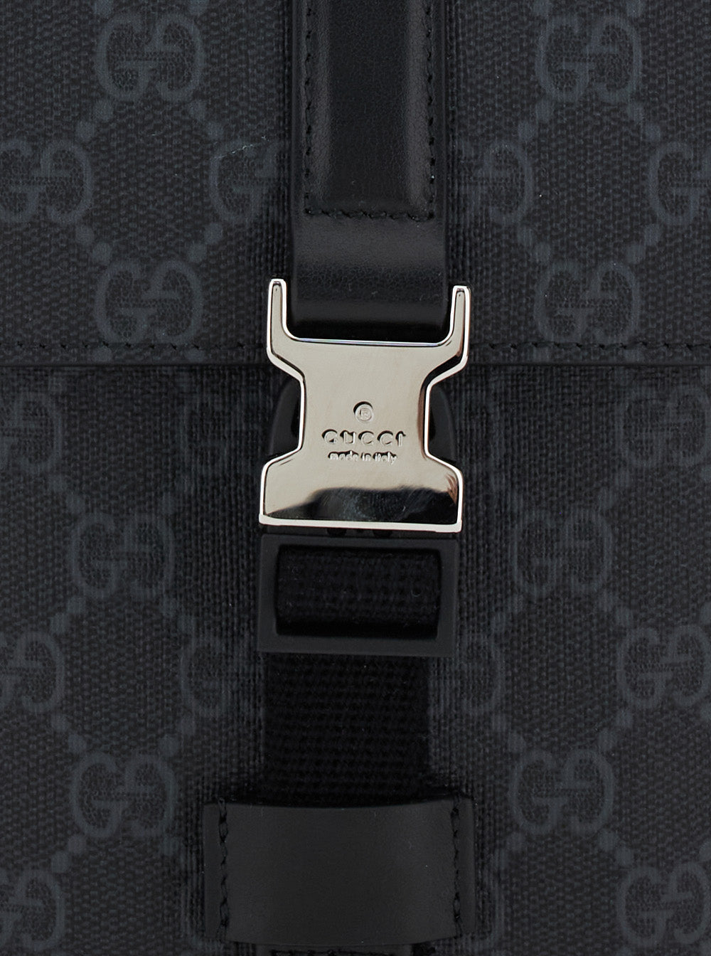 Close-up of a Gucci bag with a silver buckle on a black GG Gucci pattern background.