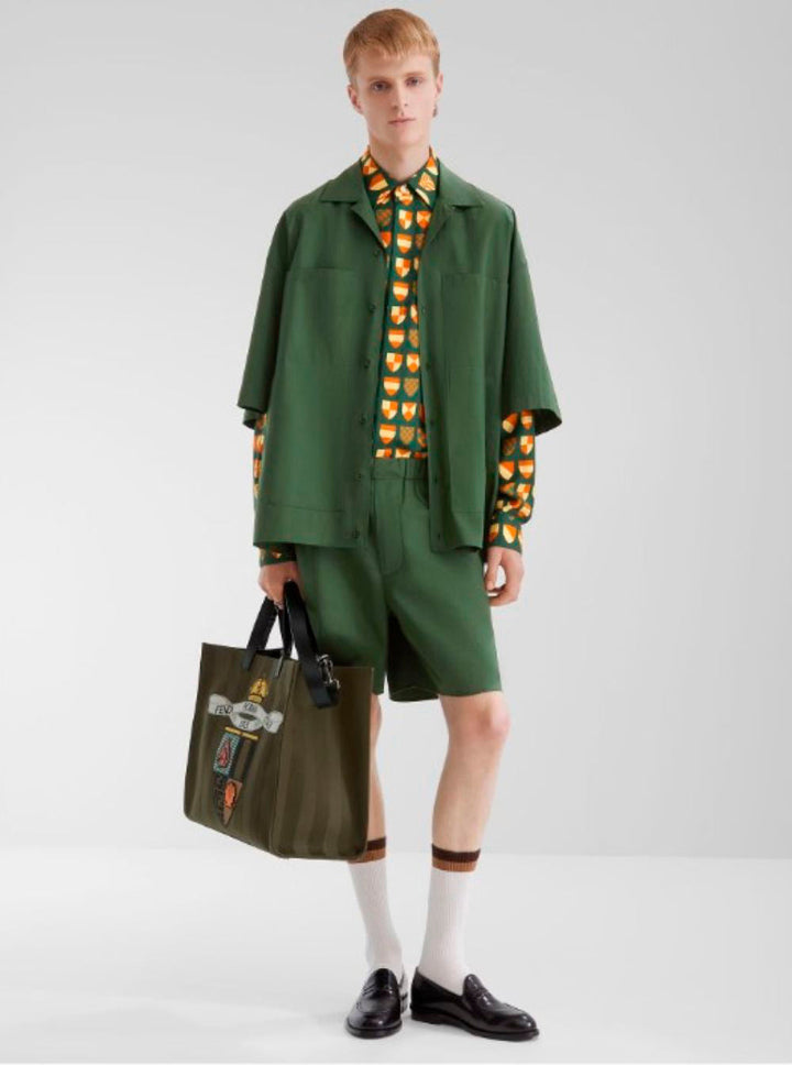 Person wearing a green outfit with a patterned shirt and holding a bag on a white background