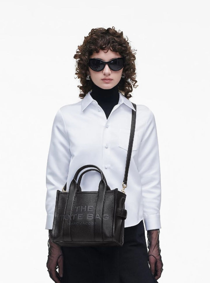 Woman holding a black handbag with 'The Kate Bag' branding on a white background