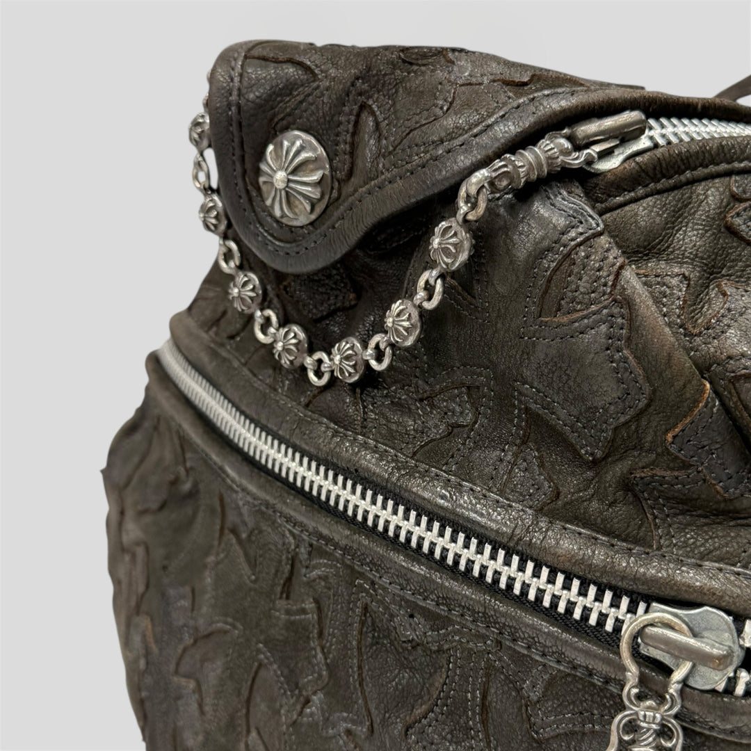 Close-up of a textured leather bag with silver chain and zipper details on a light gray background.