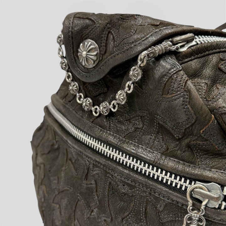 Close-up of a textured leather bag with silver chain and zipper details on a light gray background.