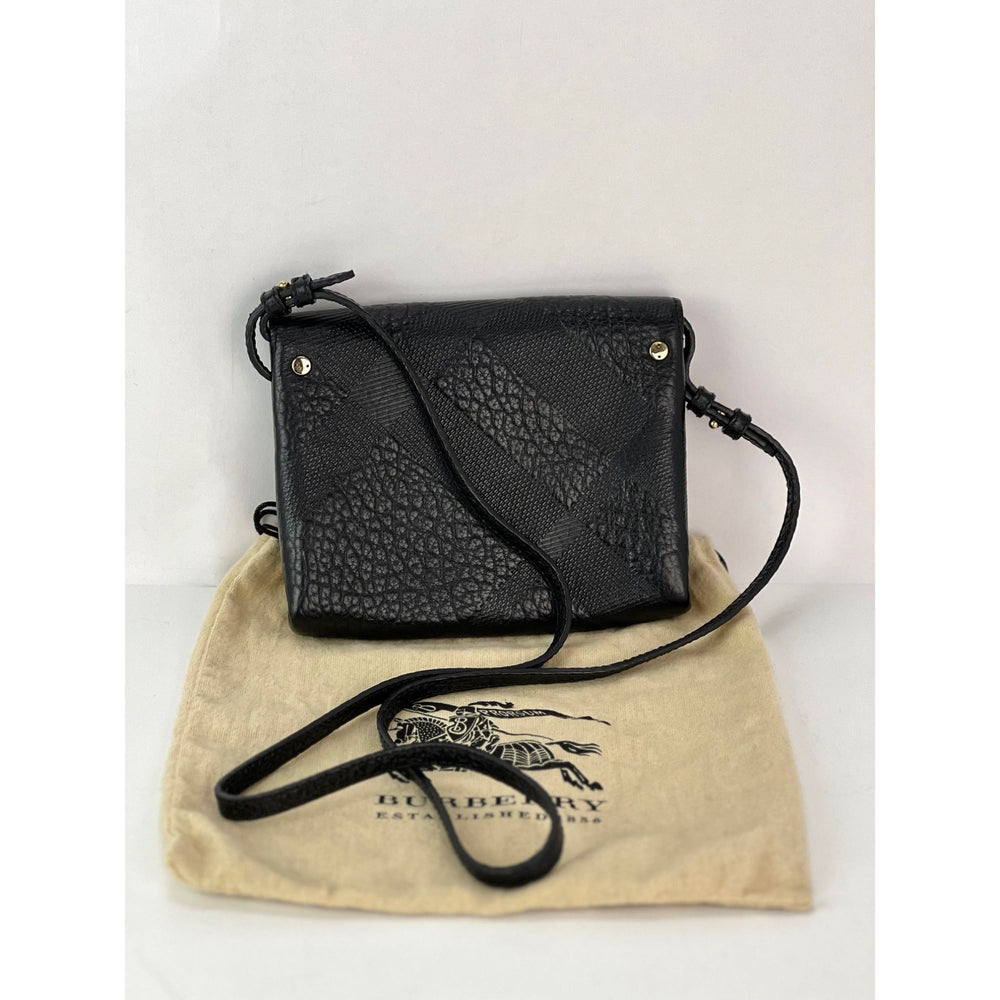 Black textured crossbody bag on a beige Burberry dust bag with a white background