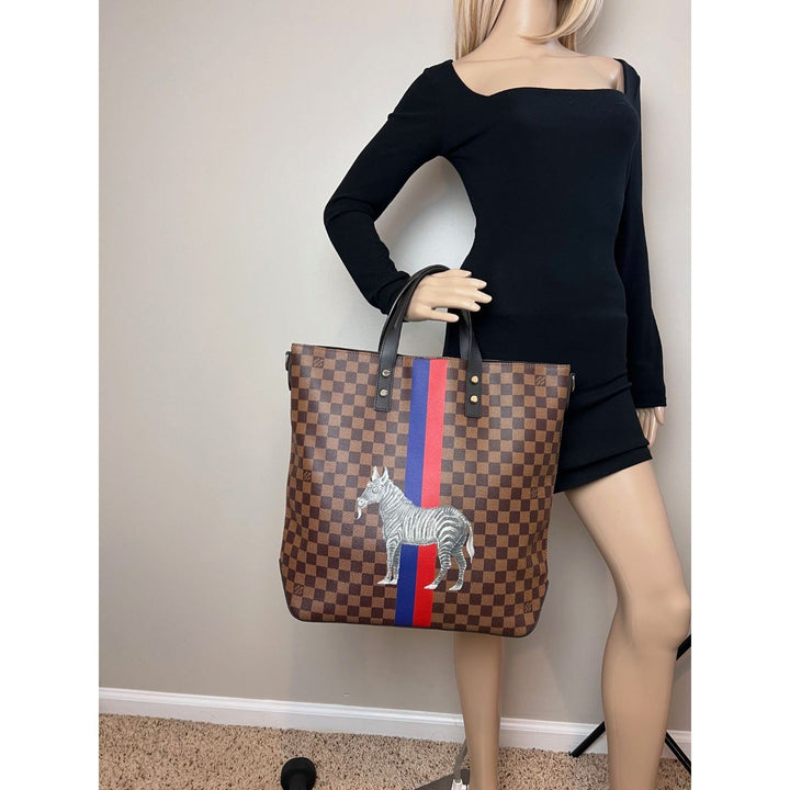 Person holding a large brown checkered tote bag with zebra design against a plain wall.
