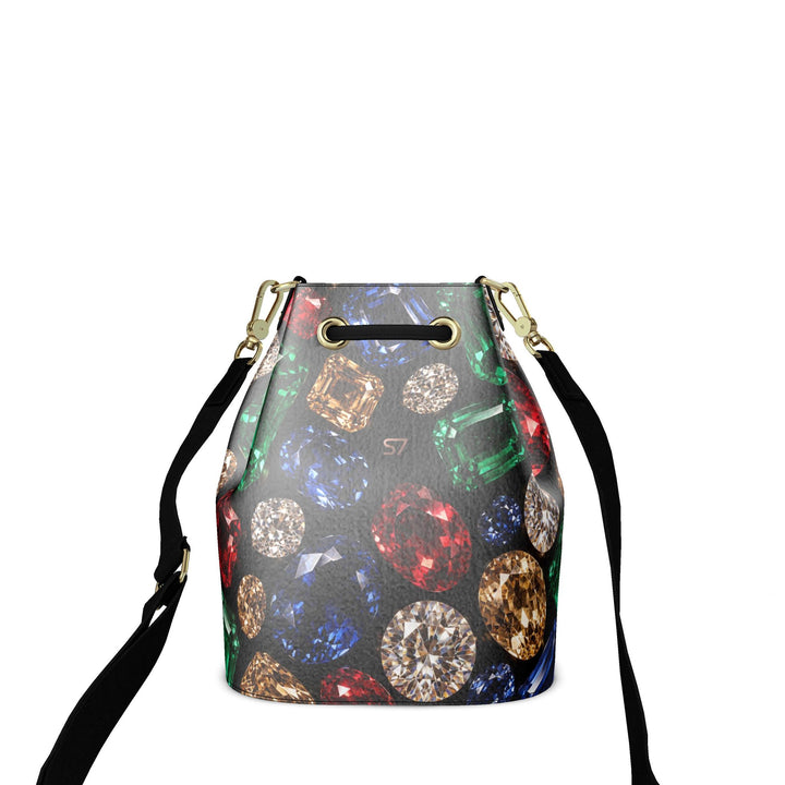 S7 Jewel Vault leather bucket bag with colorful gemstone print on black, a subtle rose-gold monogram, black shoulder strap, and gold-tone hardware.