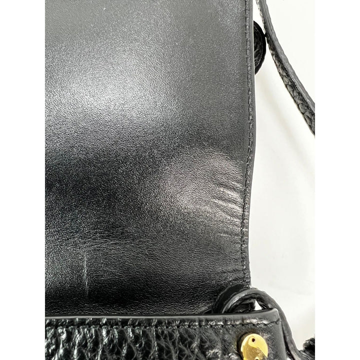 Close-up of a black leather handbag with visible wear and tear on a white background