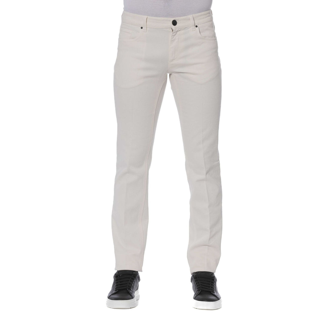 A man standing, wearing Trussardi brand beige jeans with visible logo, paired with a dark shirt and black shoes.