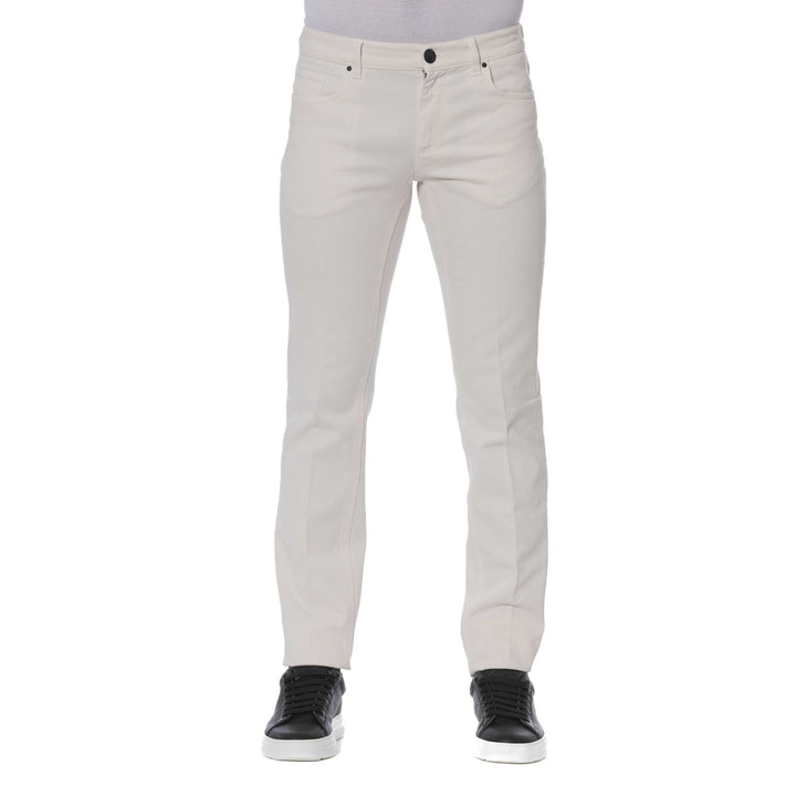A man standing, wearing Trussardi brand beige jeans with visible logo, paired with a dark shirt and black shoes.