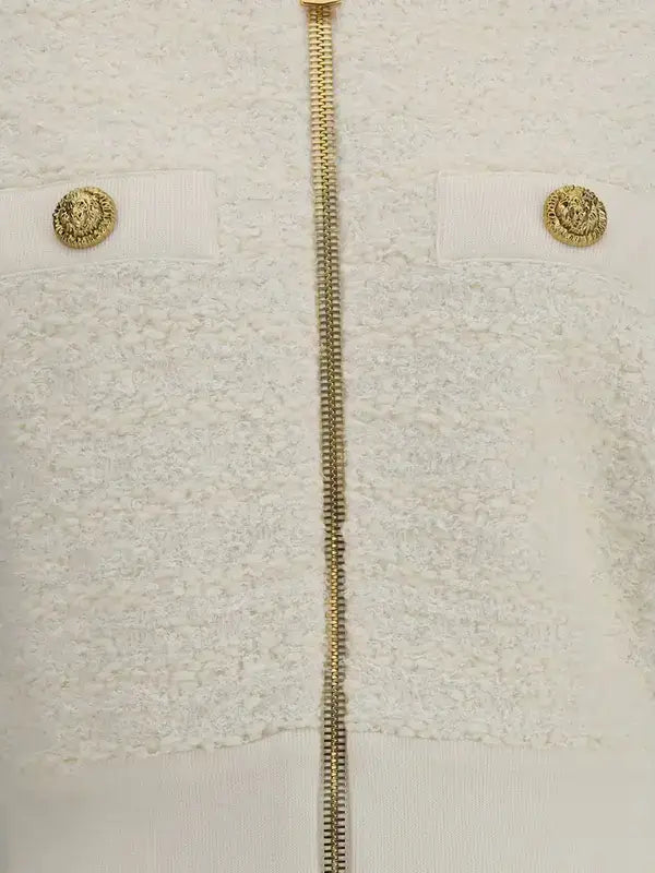 Close-up of a textured fabric with gold zipper and buttons on a light background