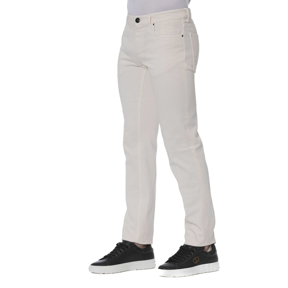 A man standing, wearing Trussardi brand beige jeans with visible logo, paired with a dark shirt and black shoes.