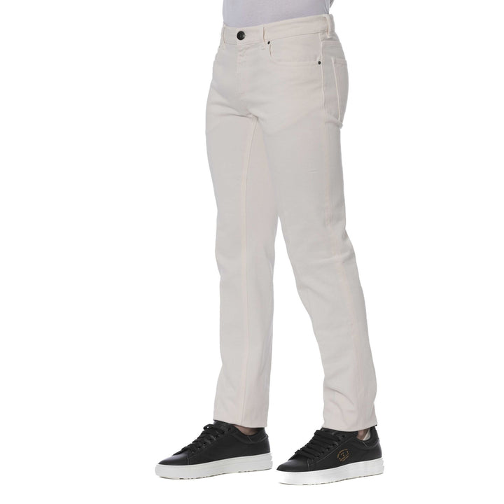 A man standing, wearing Trussardi brand beige jeans with visible logo, paired with a dark shirt and black shoes.