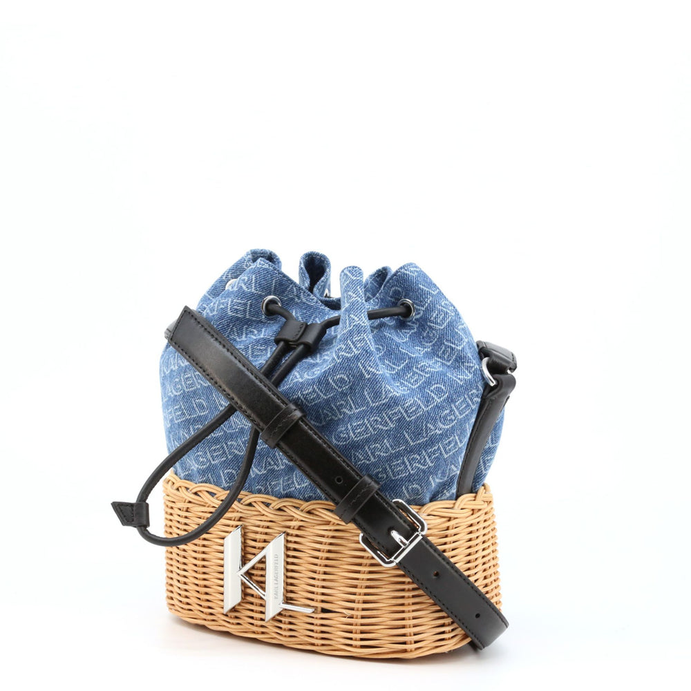 A blue Karl Lagerfeld crossbody bag with a black leather look, placed inside a wicker basket. The bag features a drawstring closure and an adjustable shoulder strap.