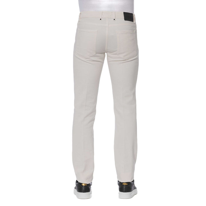 A man standing, wearing Trussardi brand beige jeans with visible logo, paired with a dark shirt and black shoes.