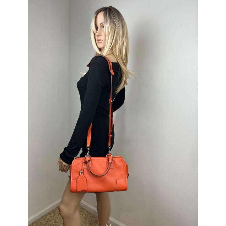 Woman holding an orange handbag against a plain background
