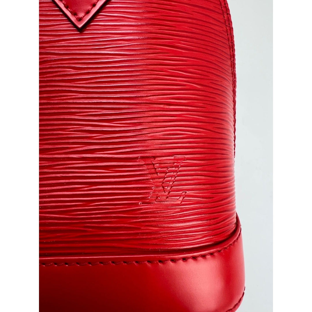 Close-up of a red textured handbag with a brand logo on a light gray background
