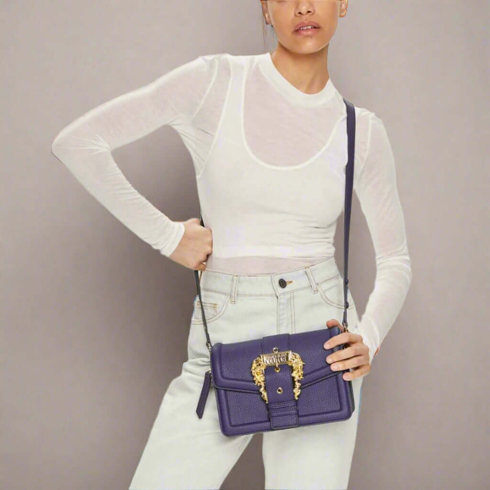 Person holding a purple handbag with decorative clasp against a white background