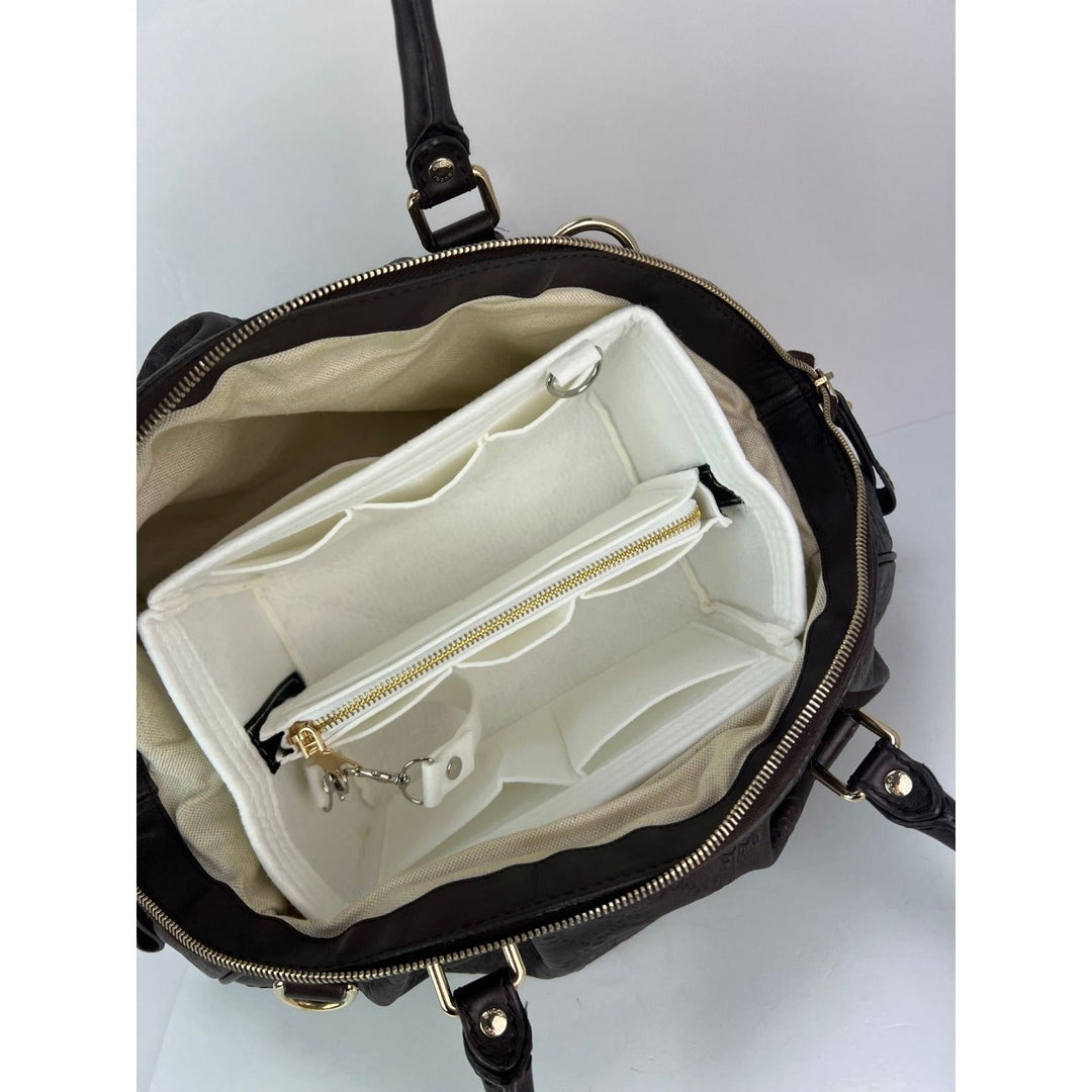 Black handbag with open interior showing beige lining on a light gray background