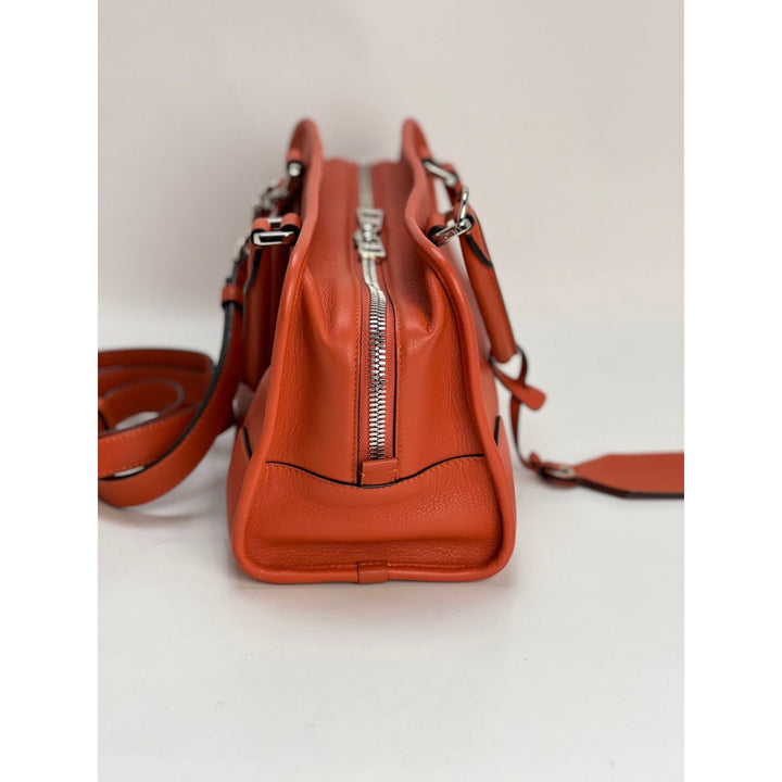 Orange leather handbag with a strap on a light gray background