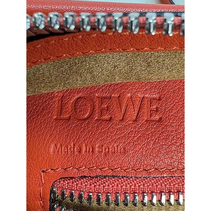 Close-up of a red leather product with 'Loewe' branding and visible stitching.
