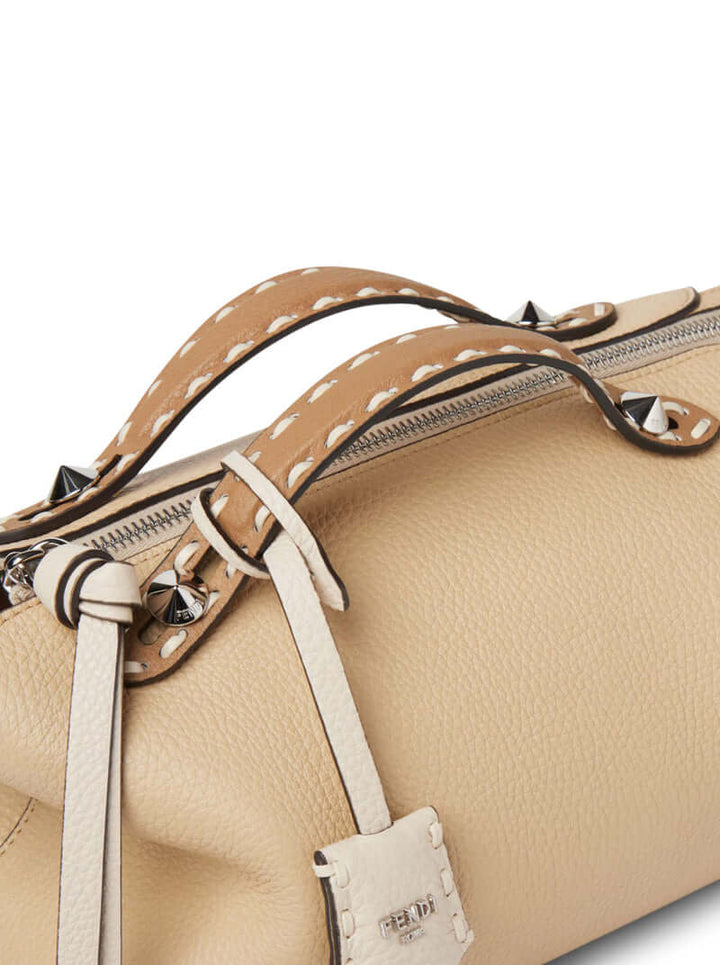 Close-up of a beige handbag with decorative straps and stitching details.