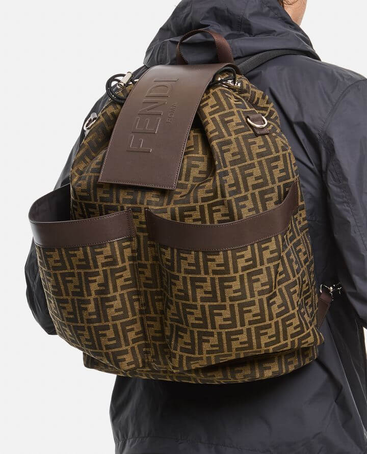 Brown patterned backpack with brown leather straps worn by a person in a dark jacket.