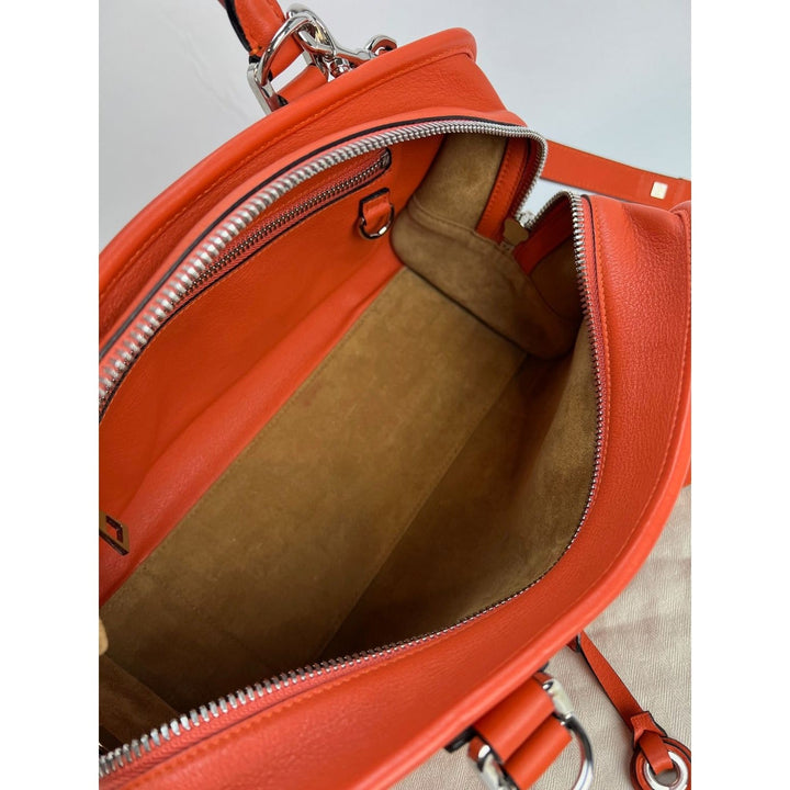 Close-up of an orange leather handbag with a visible brand logo.