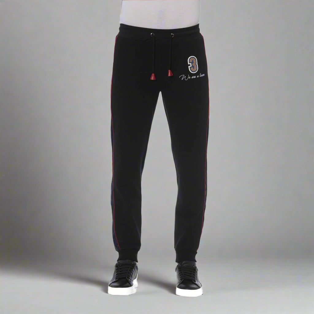 A model wearing black Trussardi tracksuit pants with red stripes on the sides and a visible logo on the left thigh.