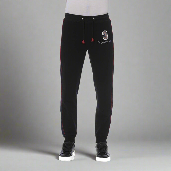 A model wearing black Trussardi tracksuit pants with red stripes on the sides and a visible logo on the left thigh.