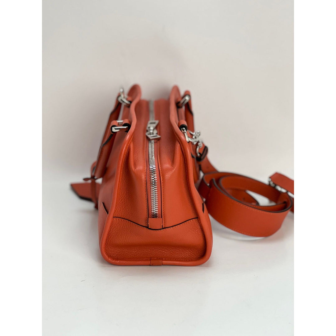 Orange leather handbag with a strap on a light gray background