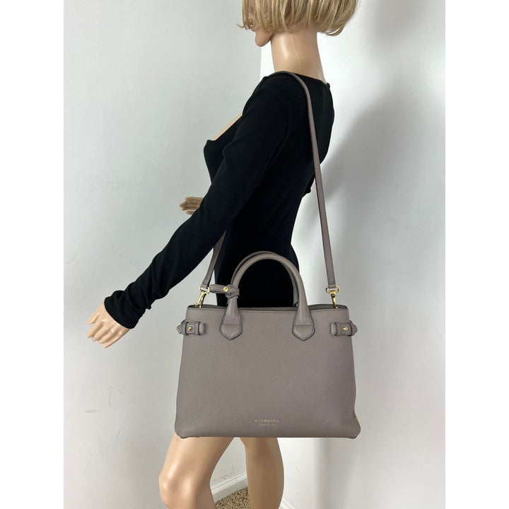 Mannequin wearing a black outfit with a gray handbag on a plain background