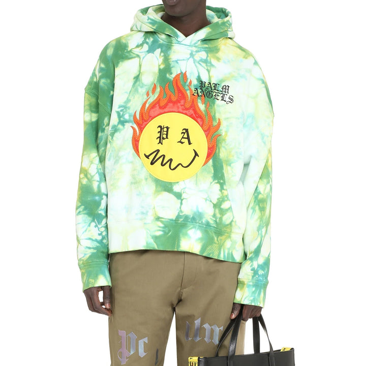 Person wearing a tie-dye hoodie with a flame design and text, holding a black bag.