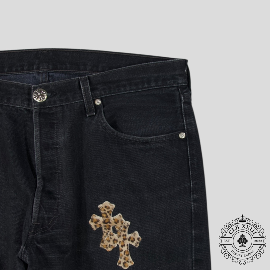 Black pants with a decorative cross patch on a gray background