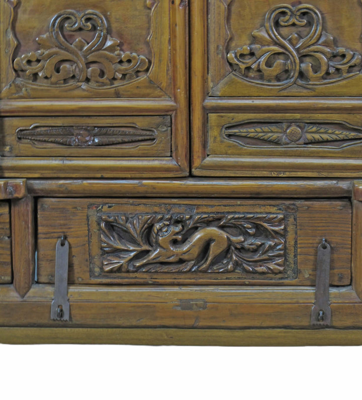 Close-up of an ornate wooden cabinet with intricate carvings and metal hooks.