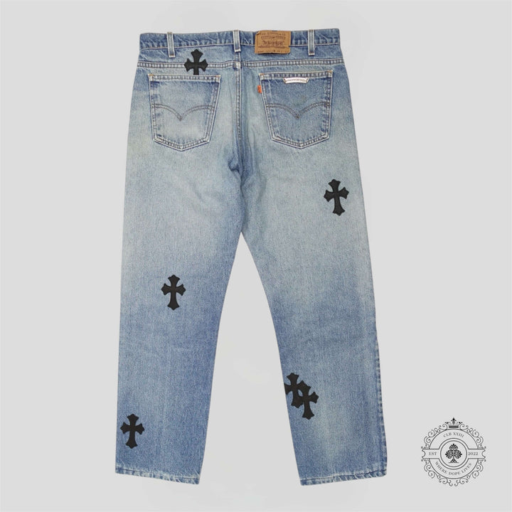 Chrome Hearts Cross Patch Jeans featuring black cross patches on a light blue denim background.