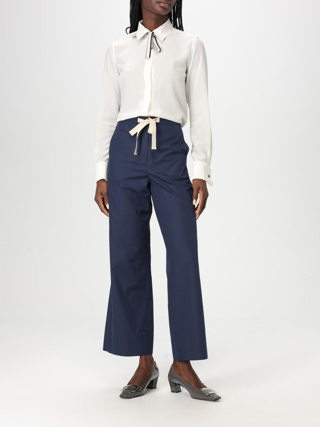Person wearing a white blouse and navy pants on a white background