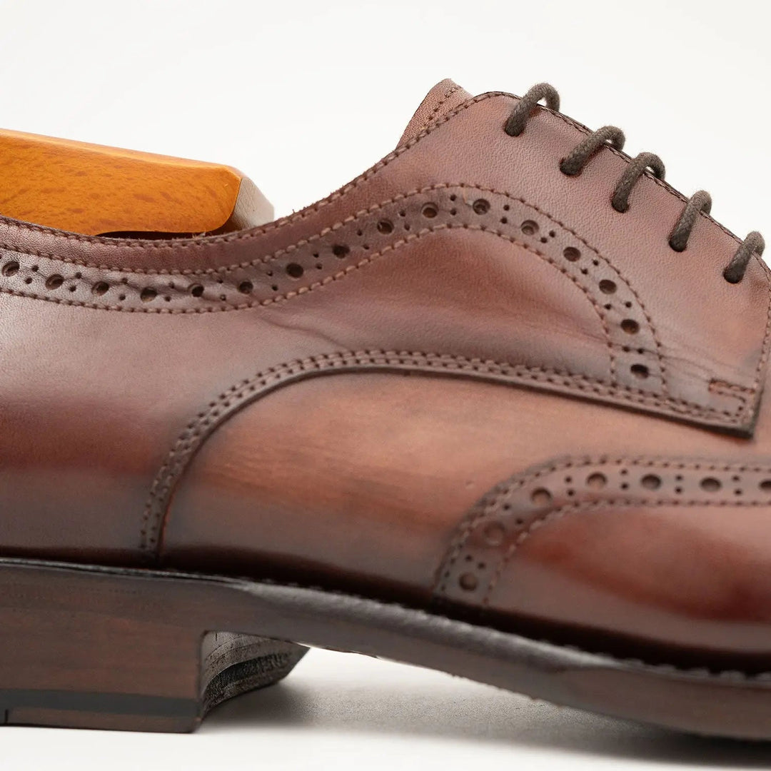 Goodyear welt derby shoes Brogue style Brown detail view, handcrafted leather, calfskin upper, featuring perforated design.