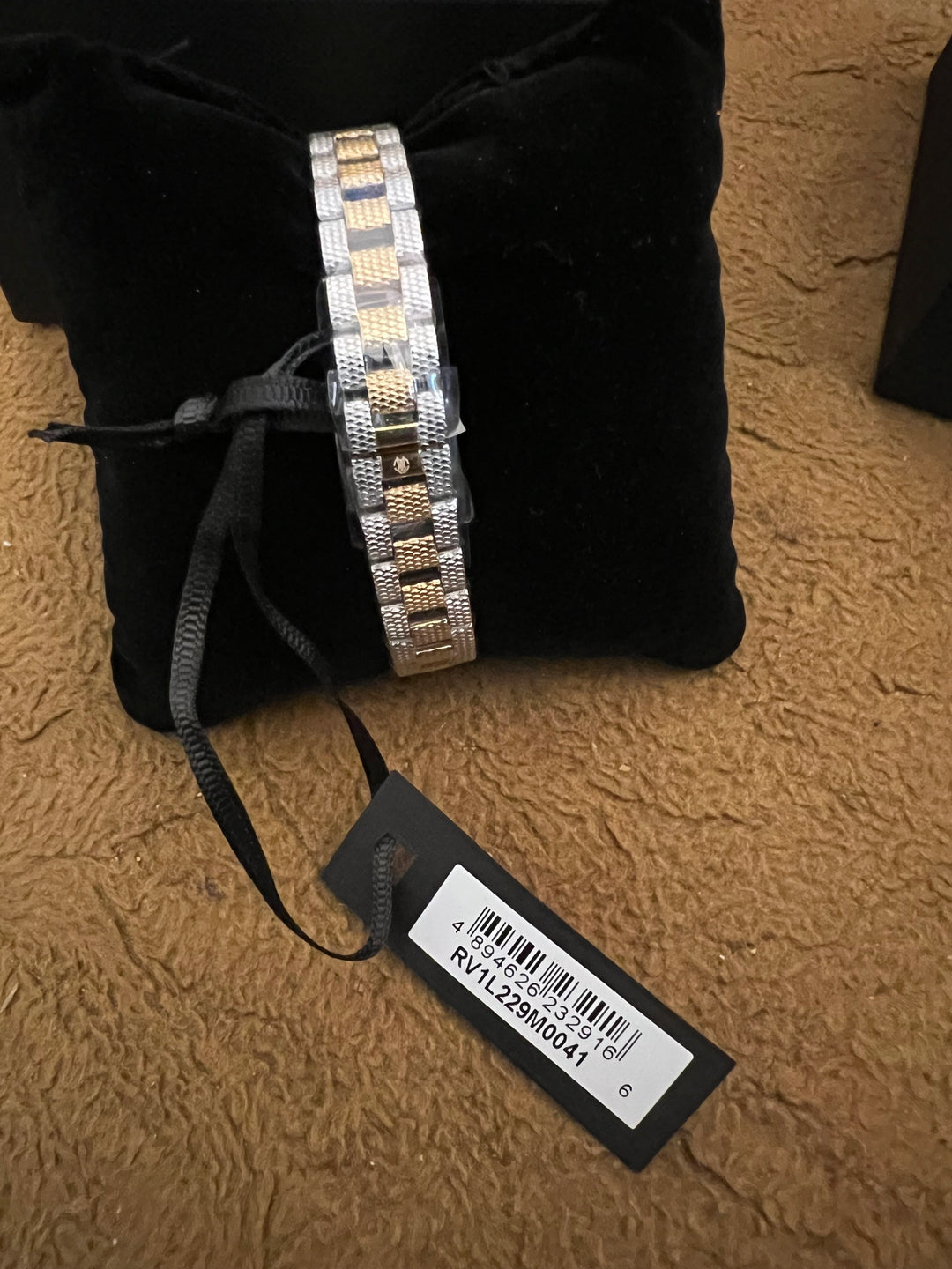 A two-tone metal link bracelet with silver and gold-colored segments, displayed on a black velvet cushion with a black price tag attached.