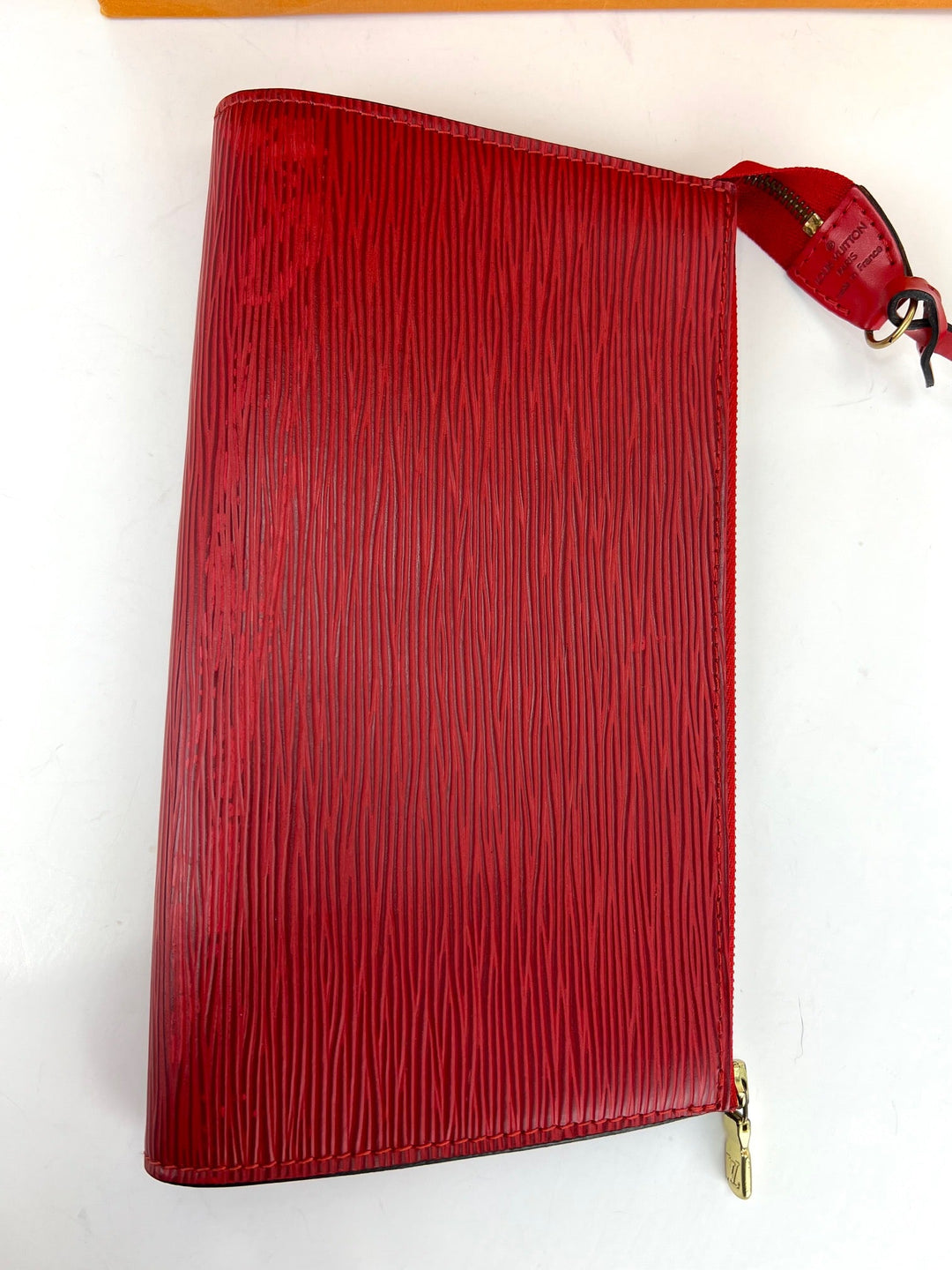 Red textured clutch bag with a gold zipper on a white background
