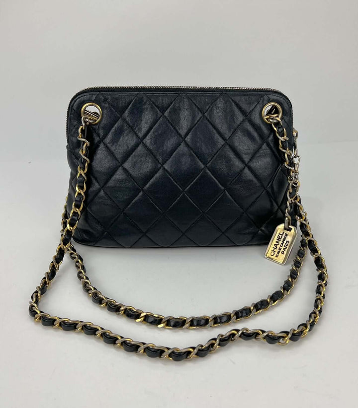 Black quilted handbag with gold chain strap on a light gray background