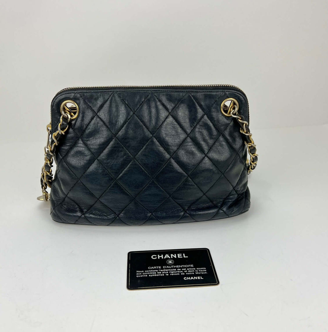 Black quilted handbag with gold chain detail on a white background, accompanied by a Chanel card.