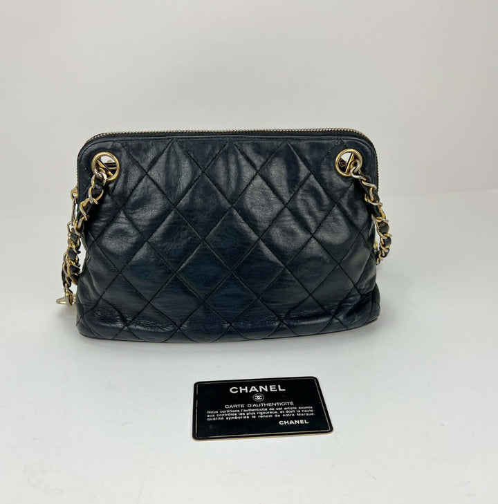 Black quilted handbag with gold chain detail on a white background, accompanied by a Chanel card.