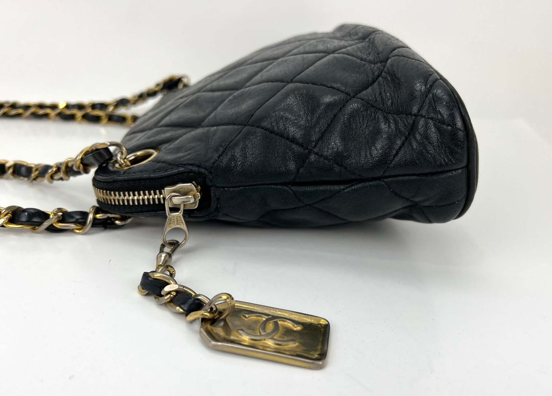 Black quilted handbag with gold chain and tag on a white background