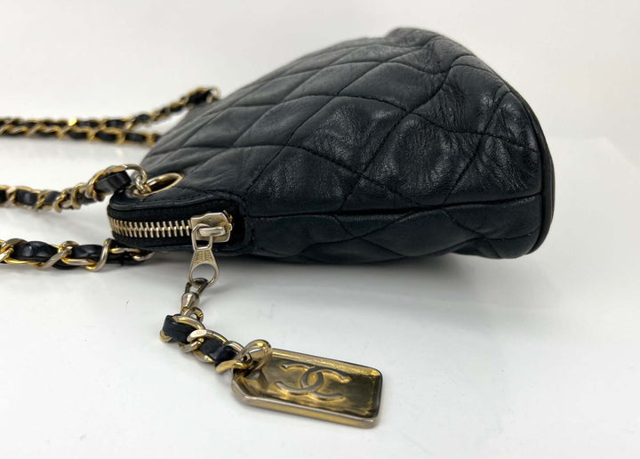 Black quilted handbag with gold chain and tag on a white background