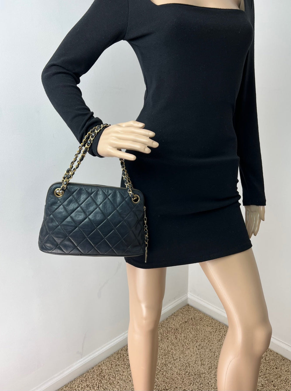 Mannequin wearing a black outfit holding a green quilted handbag against a plain background