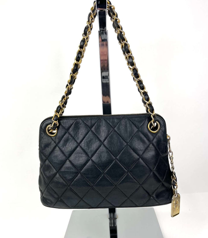 Black quilted handbag with gold chain strap on a white background