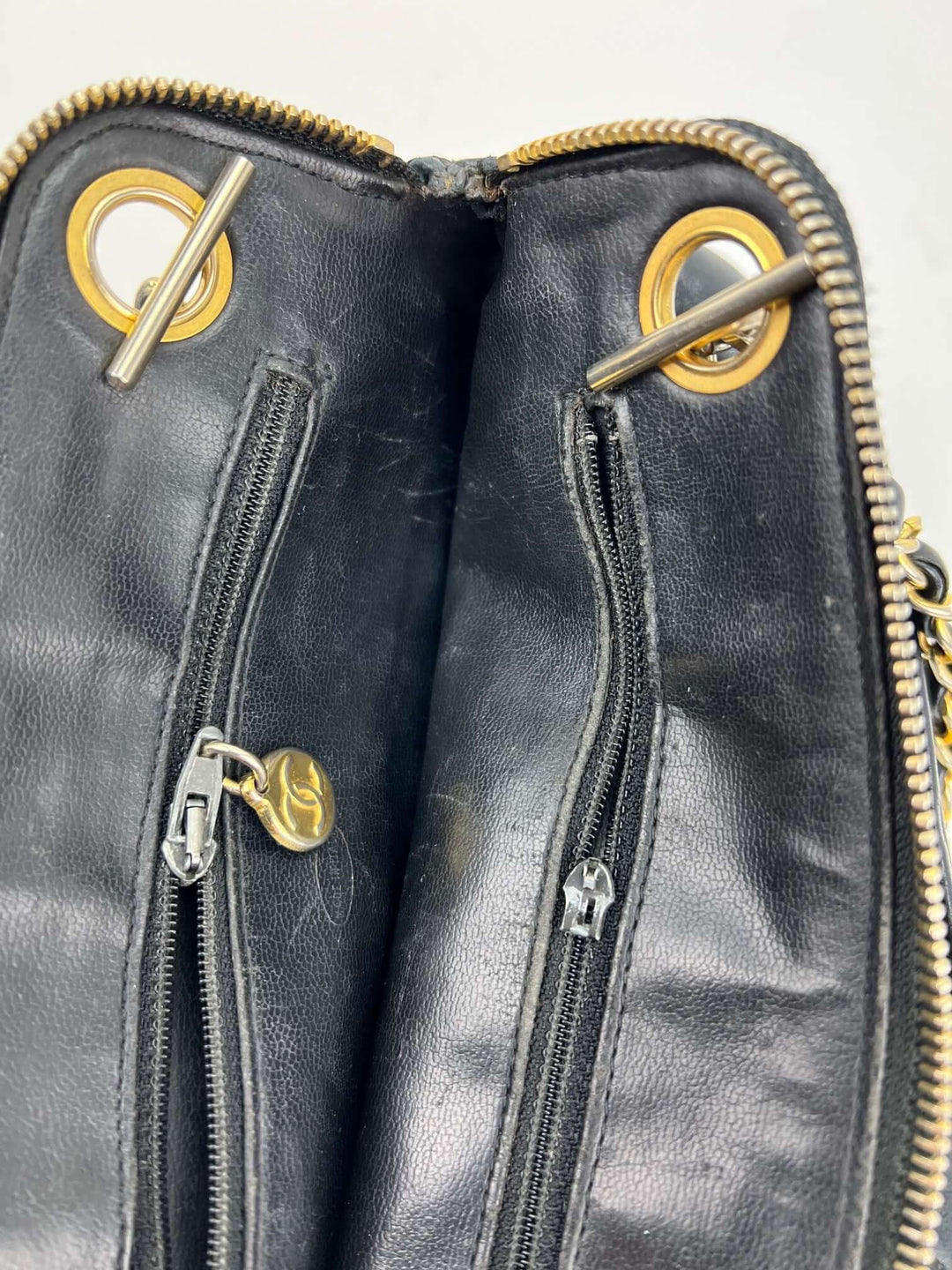 Close-up of a black leather bag with gold zippers and eyelets.