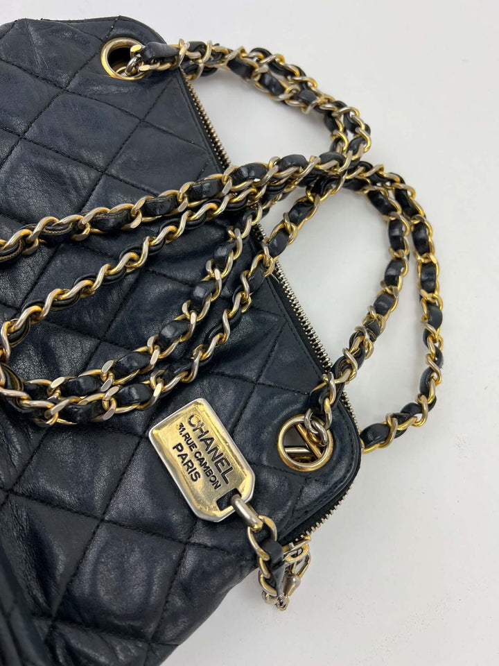 Black quilted handbag with gold chain and Chanel logo on a white background